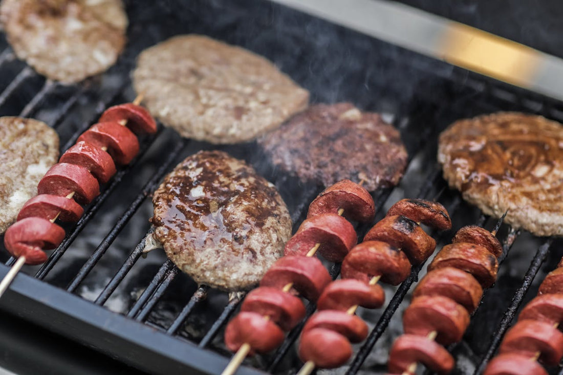 Sausages and skewered meats grilling over an open charcoal flame, illustrating the live-grill component of a Brevard County Memorial Day catering menu.