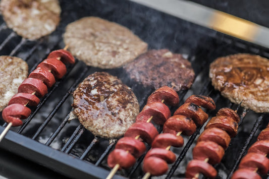 Sausages and skewered meats grilling over an open charcoal flame, illustrating the live-grill component of a Brevard County Memorial Day catering menu.