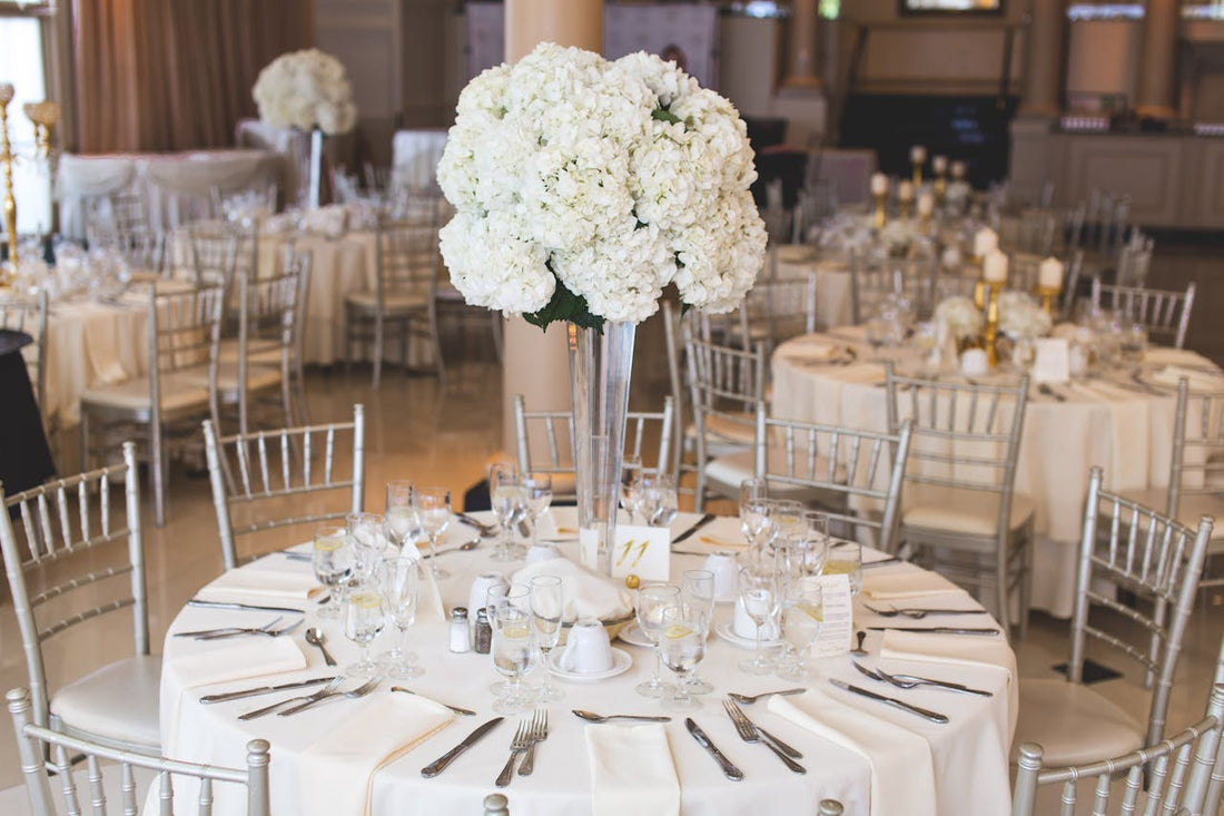 Round elegant rehearsal dinner table set with candles, glassware, and floral arrangements in a coastal venue, ready for wedding weekend guests