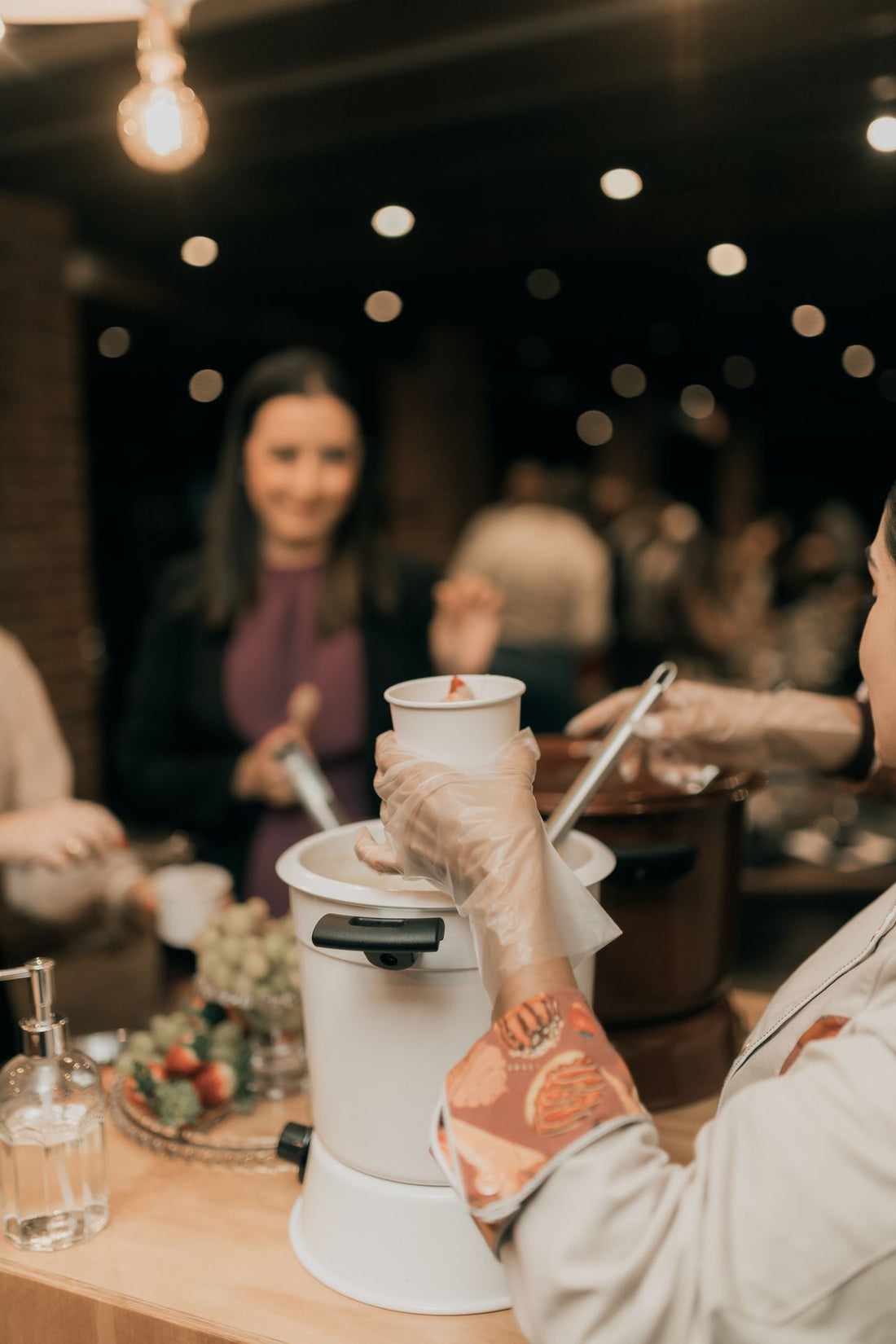 Catering staff serving food to guests at an indoor event with warm ambient lighting